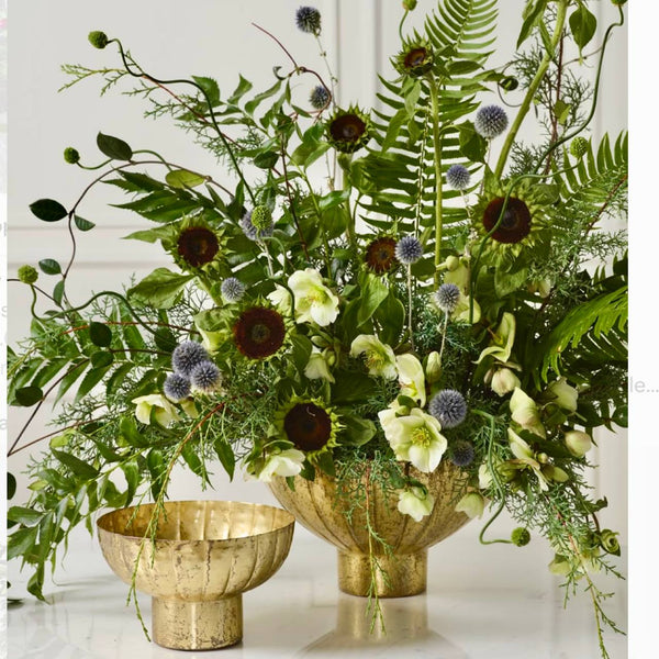 Modern corporate statement arrangement with chocolate sunflowers, blue echinops thistle, hellebores, and ferns in an antique brass compote for Los Angeles delivery.