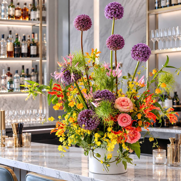 Colorful bar centerpiece with alliums, gloriosa lilies and roses on a marble bar in Los Angeles