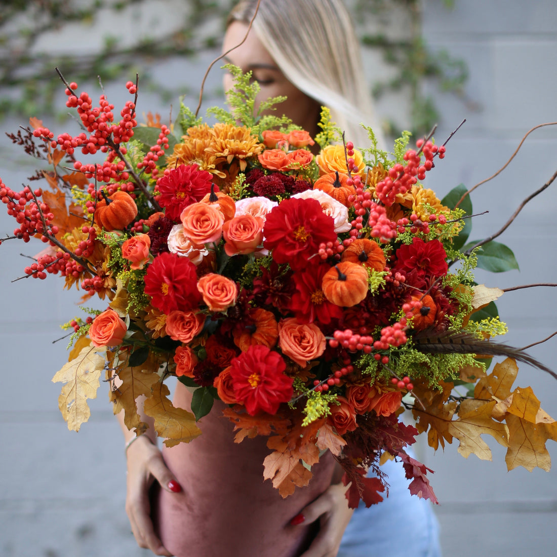 Luxurious autumn bouquet featuring red roses, dahlias, berries and mini pumpkins in a full, elegant arrangement