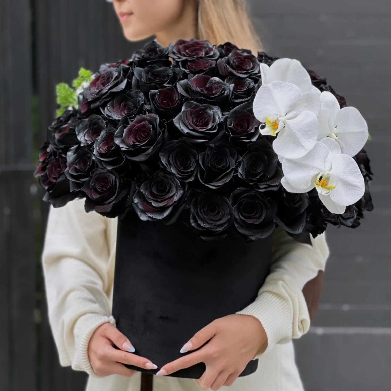 Black roses and white orchids in a精致 keepsake box, surrounded by lush greenery – a bold and elegant floral arrangement from Pink Clover LA.