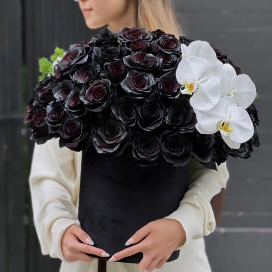 Black roses and white orchids in a精致 keepsake box, surrounded by lush greenery – a bold and elegant floral arrangement from Pink Clover LA.