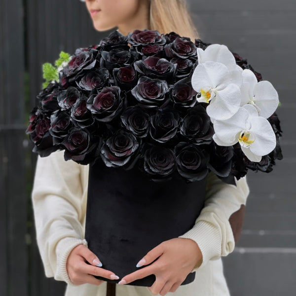 Black roses and white orchids in a精致 keepsake box, surrounded by lush greenery – a bold and elegant 