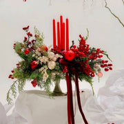 Traditional red Christmas centerpiece with red taper candles, ilex berries, mixed evergreens, red and gold ornaments, and burgundy velvet ribbon for Los Angeles delivery.