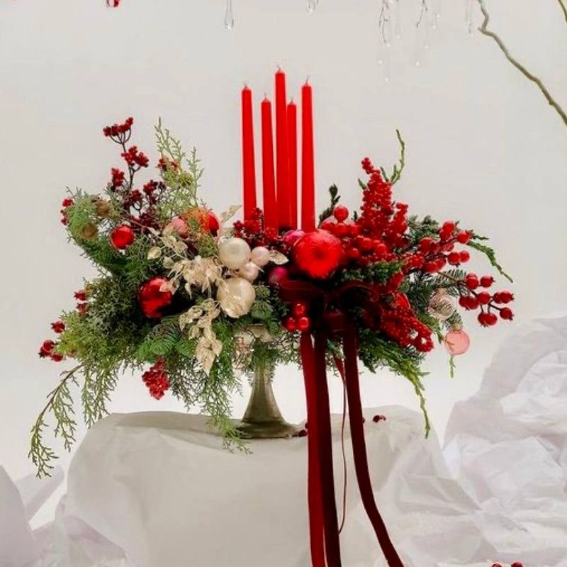 Traditional red Christmas centerpiece with red taper candles, ilex berries, mixed evergreens, red and gold ornaments, and burgundy velvet ribbon for Los Angeles delivery.