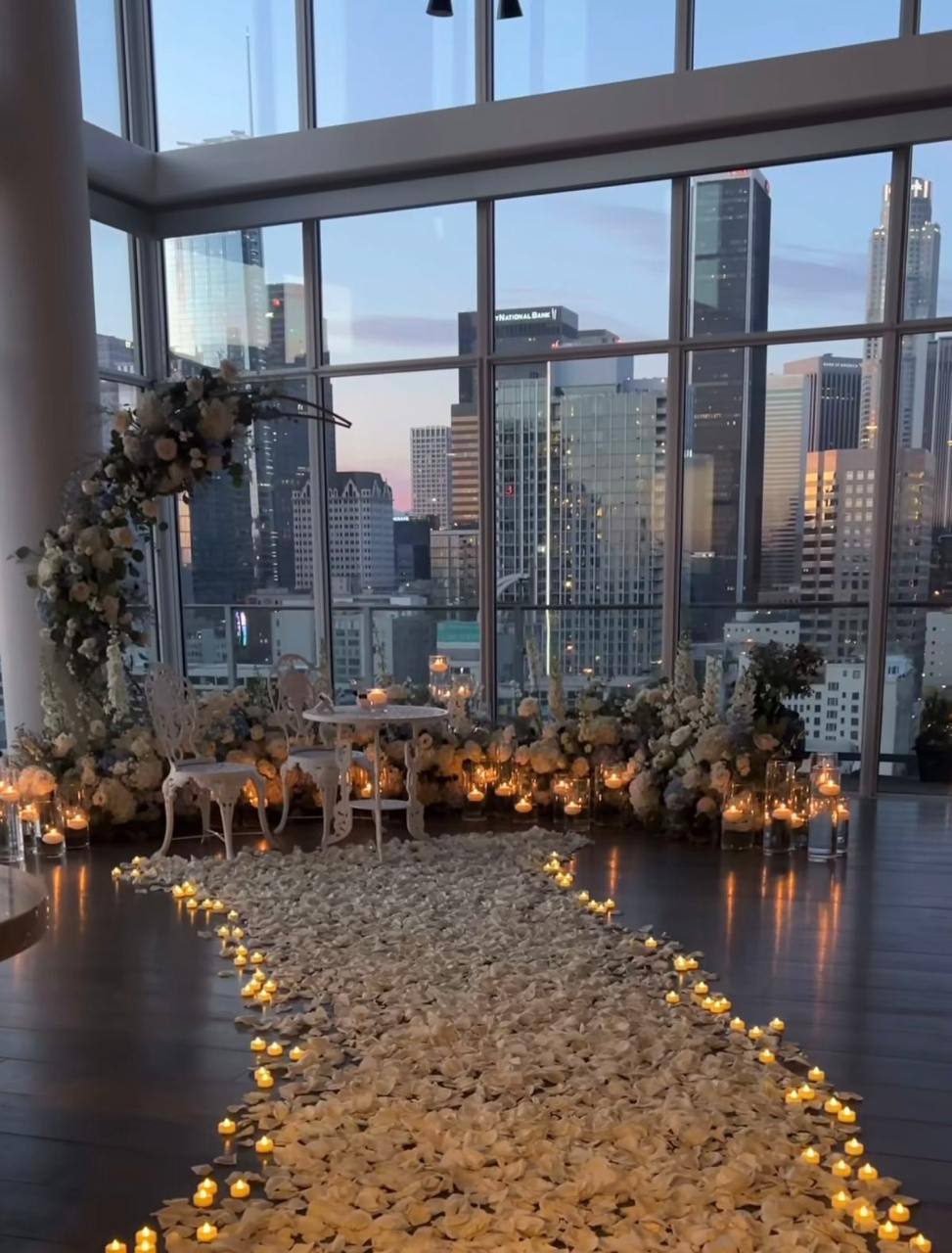 DTLA rooftop proposal aisle with floral wreath arch, ivory rose ground florals, tea light candles, white rose petal pathway, and Downtown Los Angeles skyline view.