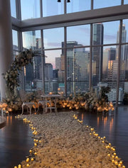 DTLA rooftop proposal aisle with floral wreath arch, ivory rose ground florals, tea light candles, white rose petal pathway, and Downtown Los Angeles skyline view.