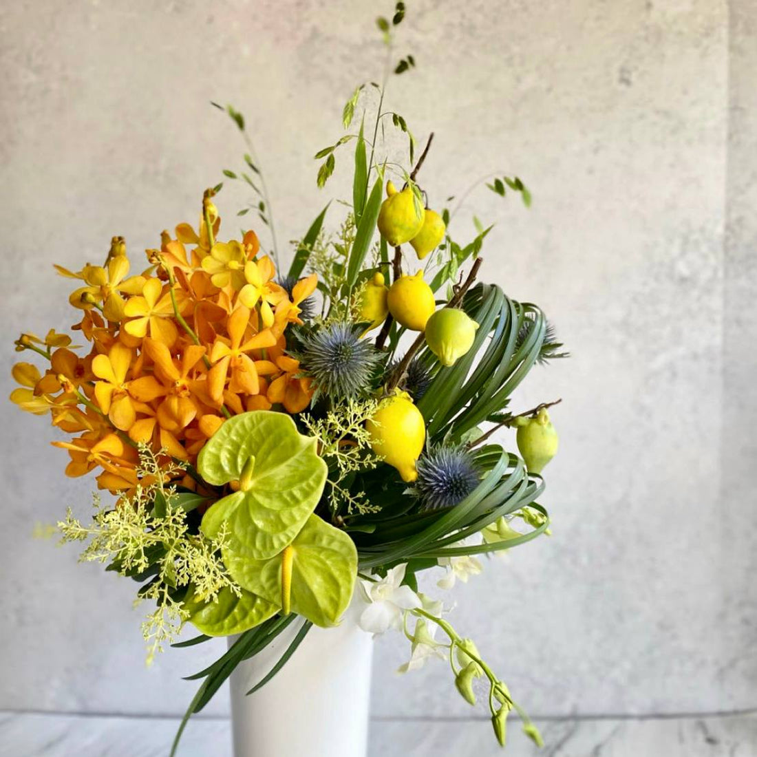 Modern tropical arrangement with golden orchids green anthuriums and ornamental citrus by Pink Clover Flowers Los Angeles
