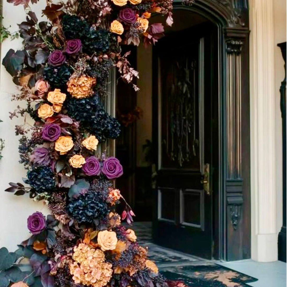 Halloween doorway garland installation with deep purple roses, peach roses, black hydrangea, and dark berries on a Los Angeles front door.