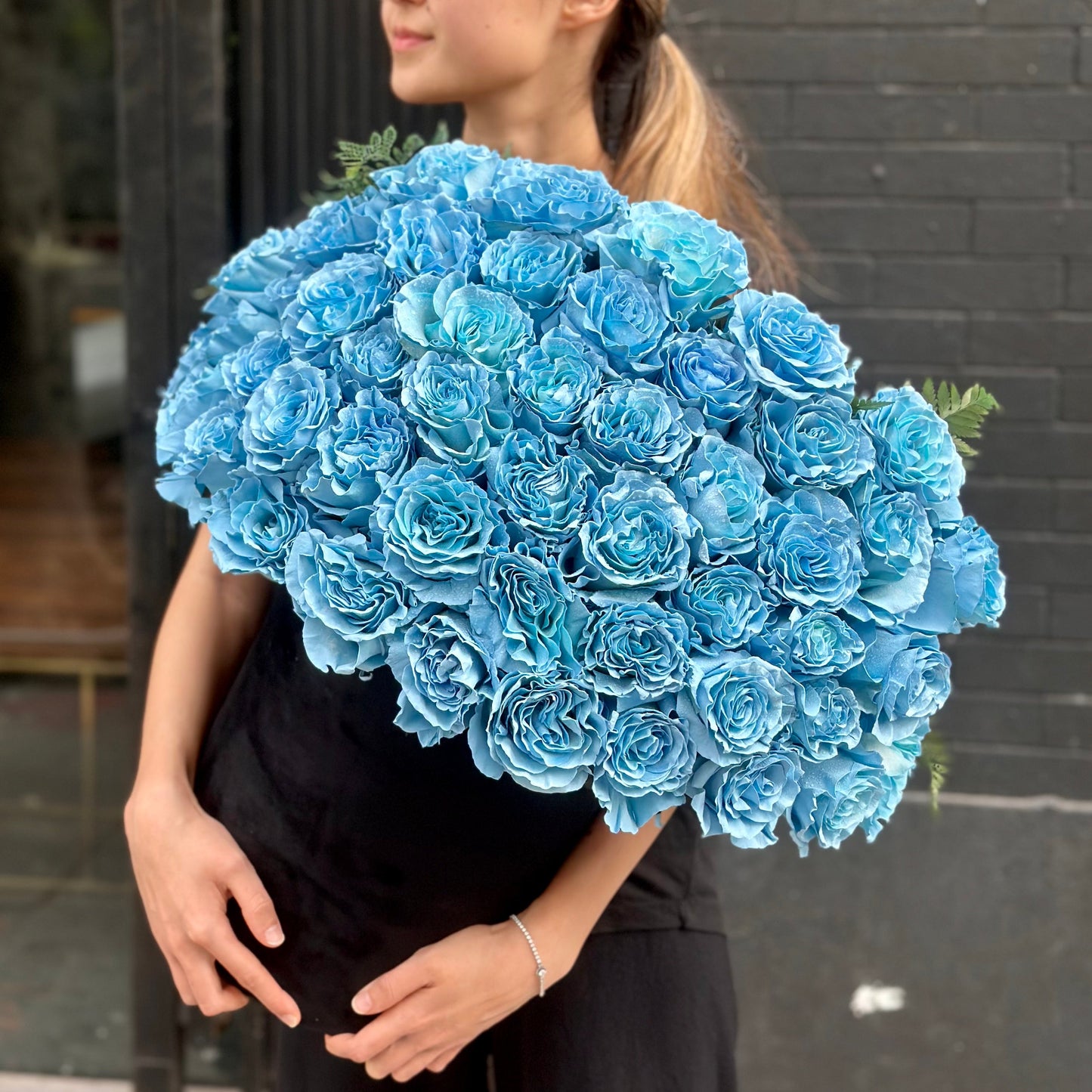 Vibrant Light Blue Roses arranged in a clear glass vase, surrounded by lush greens for a fresh, airy look.