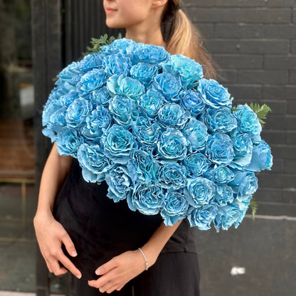 Vibrant Light Blue Roses arranged in a clear glass vase, surrounded by lush greens for a fresh, airy look.