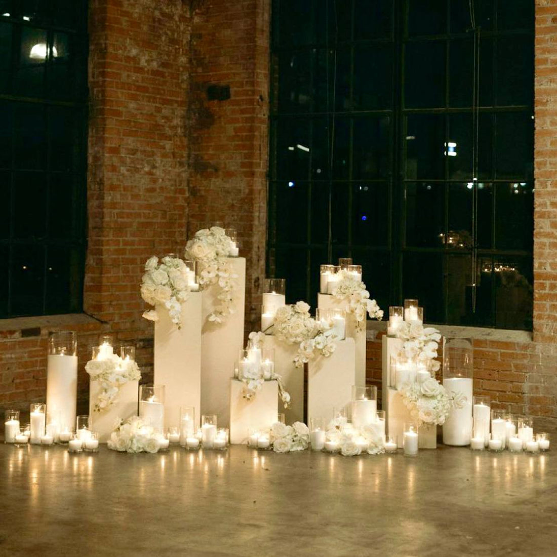 Industrial loft proposal setup with white floral pedestals, dozens of pillar candles in glass cylinders, and exposed brick architecture in Los Angeles.