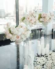 Pair of ivory and blush rose centerpieces on white fluted pedestals with acrylic stands and floating candles for a Los Angeles proposal setup.