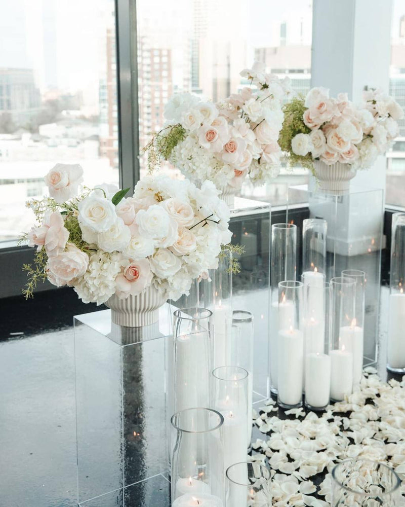 Pair of ivory and blush rose centerpieces on white fluted pedestals with acrylic stands and floating candles for a Los Angeles proposal setup.