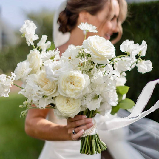 Ivory garden bridal bouquet with white roses, sweet peas, and stocks held by bride outdoors in Los Angeles