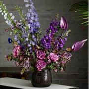 Purple and lavender Halloween arrangement with delphinium, anthurium, stock, and garden roses in a dark vessel for Los Angeles delivery.