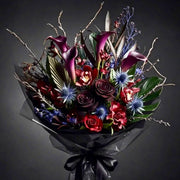 Dark Halloween hand-tied bouquet with black calla lilies, deep red cymbidium orchids, blue eryngium thistle, and twisting branches in black wrap.