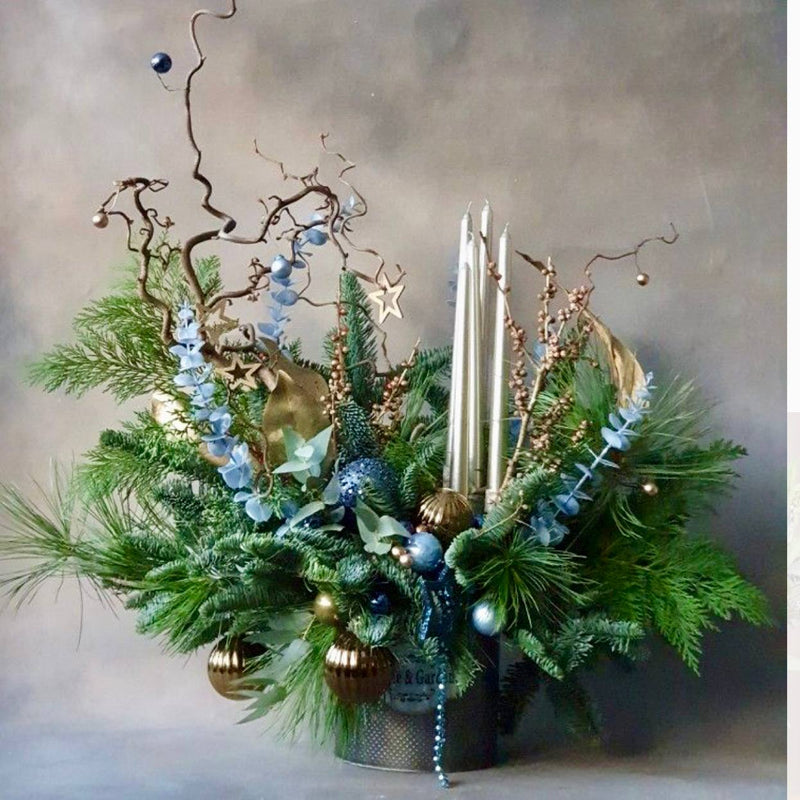 Christmas centerpiece with pine, blue eucalyptus, gold ornaments, blue baubles, twisted branches, and silver tapers for Los Angeles holiday delivery.