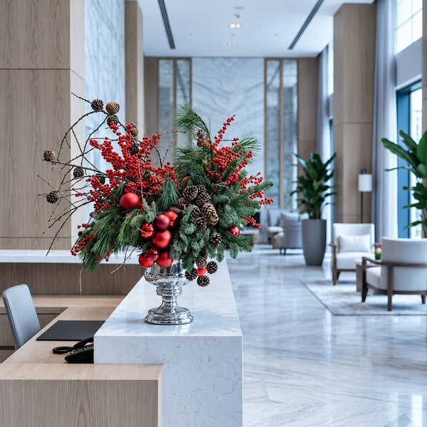 Christmas lobby arrangement of pine, winterberry and red ornaments in a silver urn on a reception desk in Los Angeles