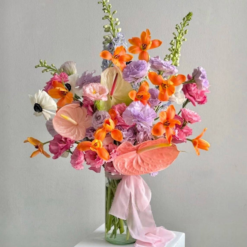 Pastel tropical bouquet with peach and pink anthurium, lavender lisianthus, orange ornithogalum, white anemone, and pink ribbon for Los Angeles delivery.