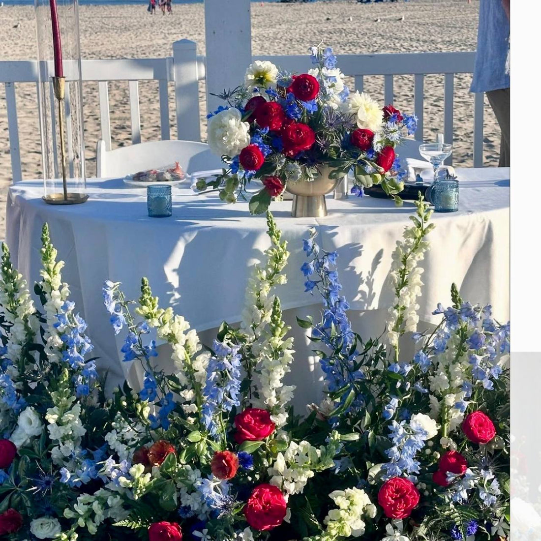 4th of July sweetheart table setup on Santa Monica beach with red, white, and blue centerpiece, candles, and ground florals.