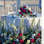 4th of July sweetheart table setup on Santa Monica beach with red, white, and blue centerpiece, candles, and ground florals.