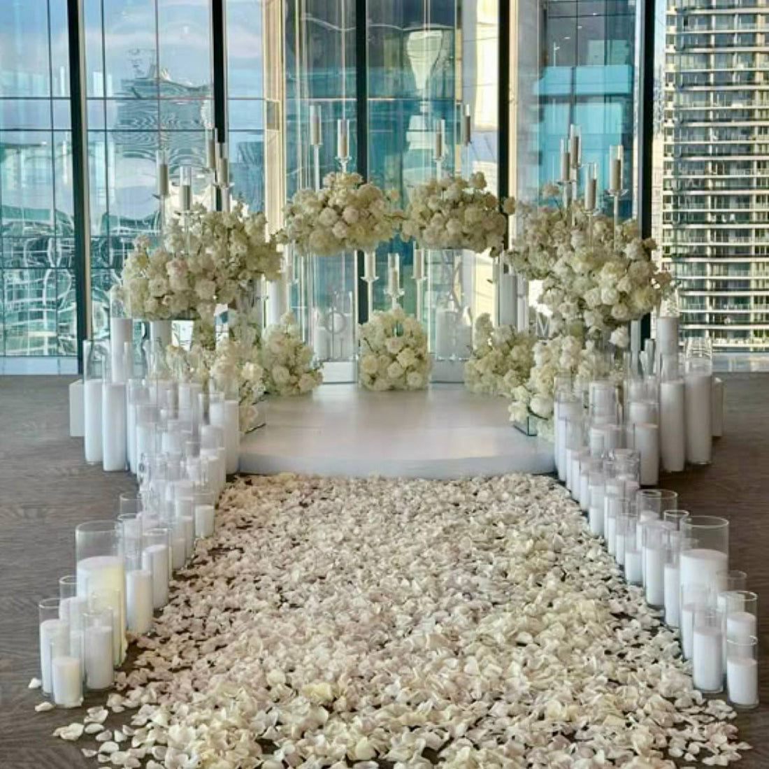 Penthouse proposal aisle with ivory rose arch installation, dense pillar candles in glass cylinders, and white rose petal pathway with Los Angeles skyline view.