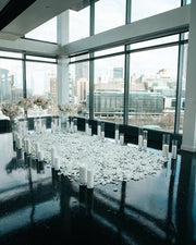 Penthouse proposal setup with twin floral pedestals, white rose petal aisle, and double row of glass cylinder candles with Los Angeles skyline view.