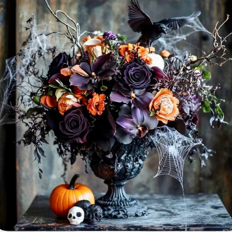 Gothic Halloween centerpiece with black orchids, deep purple roses, peach roses, raven, skull, spider webs, and pumpkin for Los Angeles delivery.