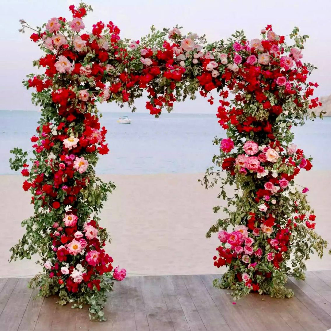 Lush red and pink rose wedding arch with greenery at a beachfront ceremony in Los Angeles