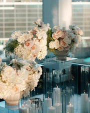 Three white and blush rose pedestal centerpieces with cymbidium orchids on acrylic stands with floating candles for a luxury Los Angeles proposal.