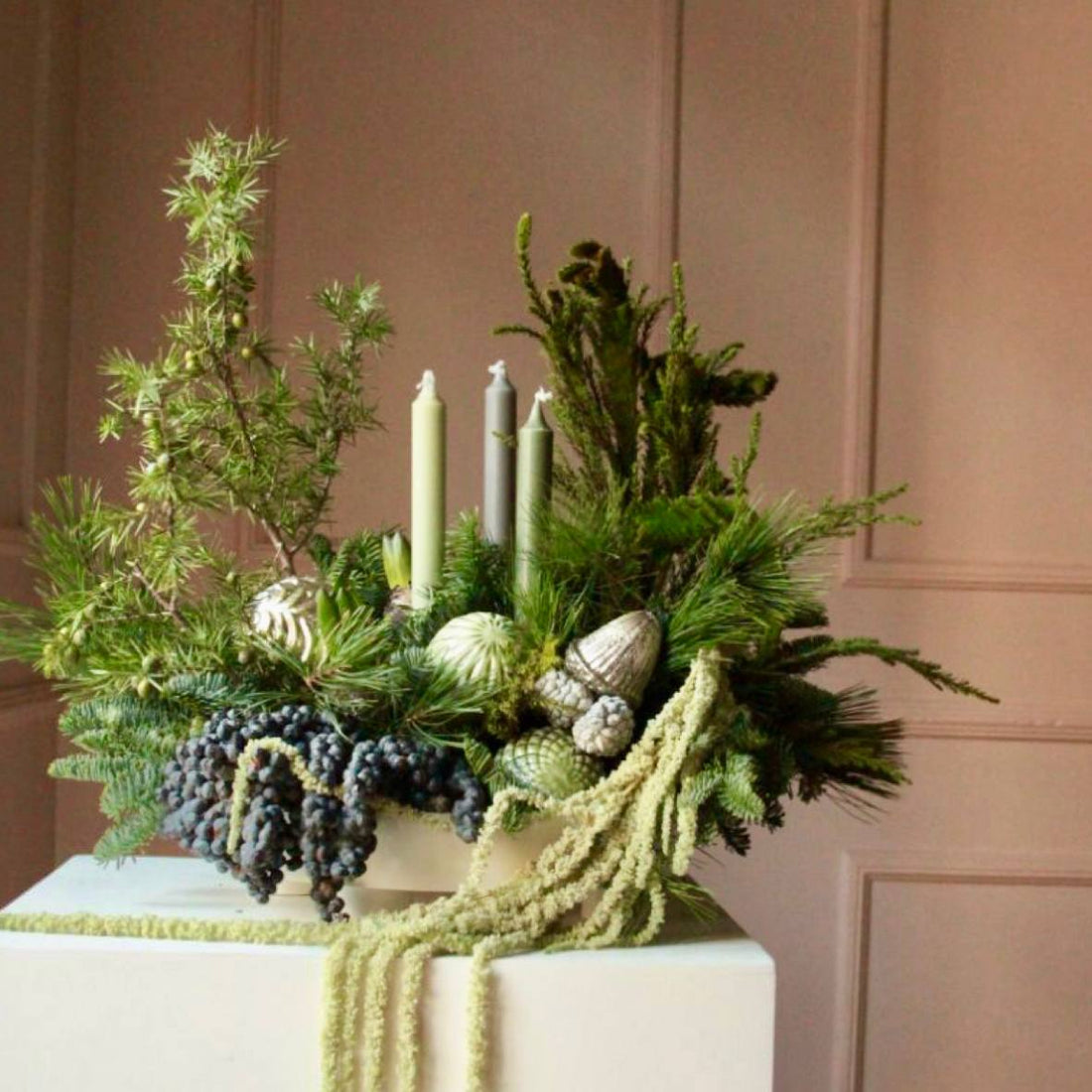 Modern sage green Christmas centerpiece with evergreens, juniper, pinecones, sage taper candles, and dried amaranthus for Los Angeles delivery.
