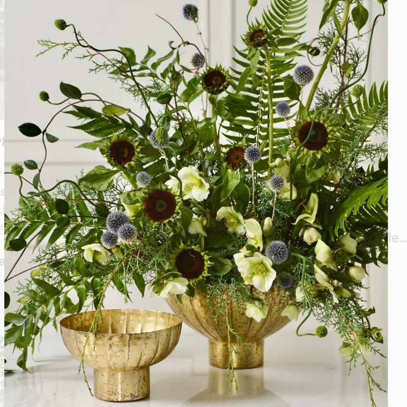 Modern corporate statement arrangement with chocolate sunflowers, blue echinops thistle, hellebores, and ferns in an antique brass compote for Los Angeles delivery.