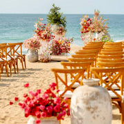 Beach wedding ceremony with terracotta urn pedestals and vibrant pink and coral floral installations on the sand in Los Angeles.