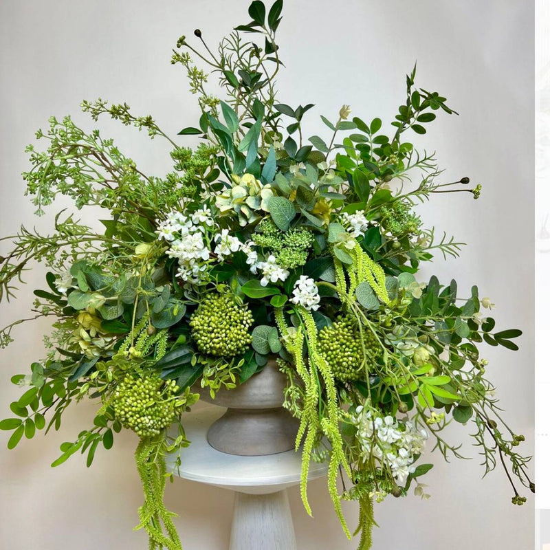 Modern all-greenery corporate centerpiece with sedum, eucalyptus, trailing amaranthus, and white blooms in a stone pedestal vase for Los Angeles delivery.