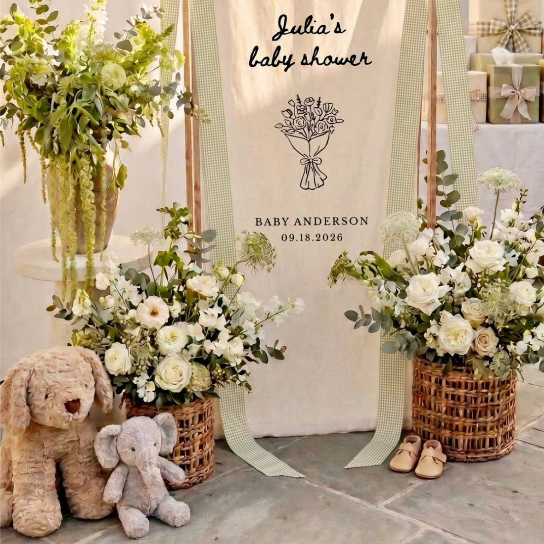 Neutral baby shower welcome scene with custom linen sign ribbon, ivory rose baskets, eucalyptus, and plush animals for Los Angeles delivery.