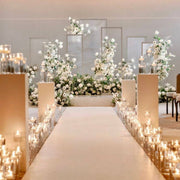 White ceremony aisle setup with dense pillar candle rows in glass cylinders, white floral installation, and modern frame backdrops for Los Angeles wedding or proposal.