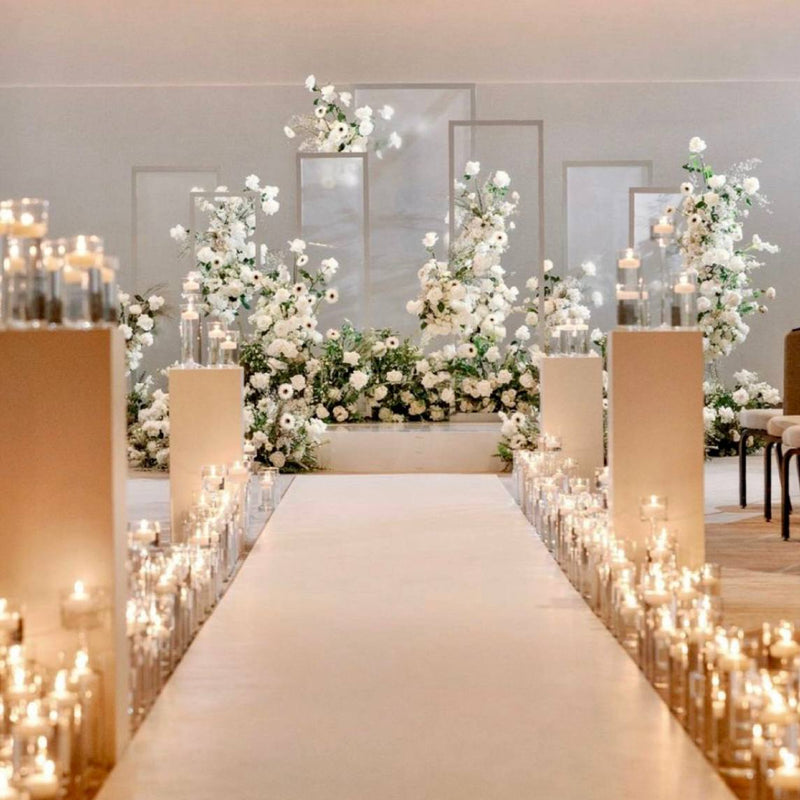 White ceremony aisle setup with dense pillar candle rows in glass cylinders, white floral installation, and modern frame backdrops for Los Angeles wedding or proposal.