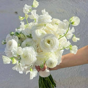 Pure white ranunculus and sweet pea bridal bouquet held against a minimalist background in Los Angeles
