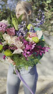 Soft pink and white floral arrangement with lush foliage, presented in a delicate wrap for a premium gifting style