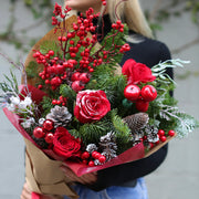 Festive Christmas bouquet featuring red roses, pine branches, and pinecones arranged in a decorative